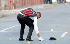 A policeman places markers at a crime scene on Delamere Avenue, St Andrew - Image via jamaica-gleaner.com