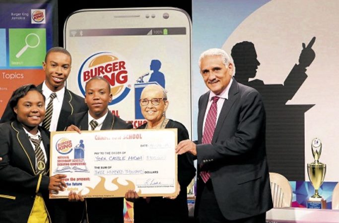 The York Castle High team — Kadijah Cox (left), Michael Miller (second left) and Danmar Clarke (centre) — collect their Champion's cash prize of $300,000 from Lois Sherwood, Chairman, Restaurant Associates Ltd and Richard Lake, Group CEO. - Image via jamaicaobserver.com